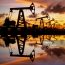 Pump jack silhouette against a sunset sky with reflections in the water.